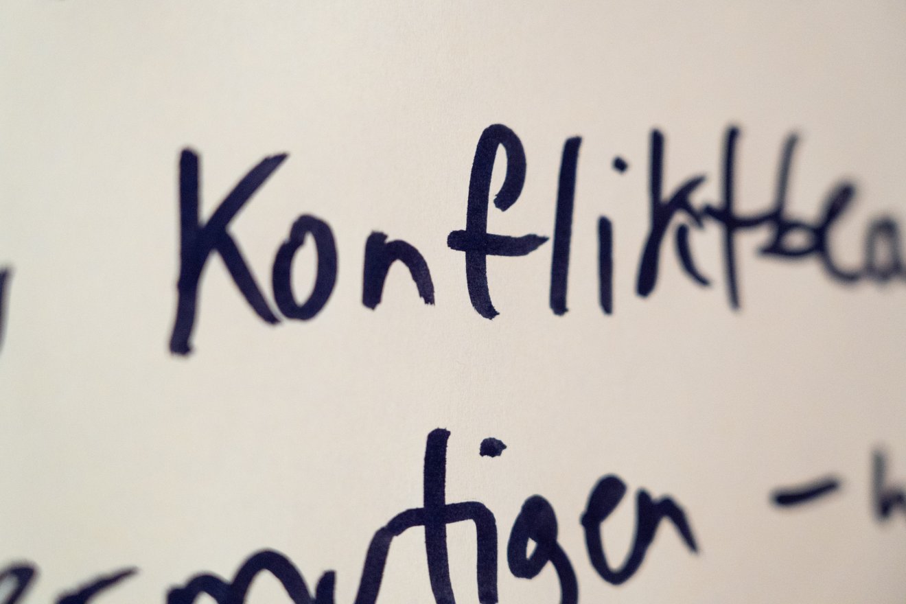 Das Wort "Konflikt" hangeschrieben im Fokus des Bildes, der Rest verschwimmt.