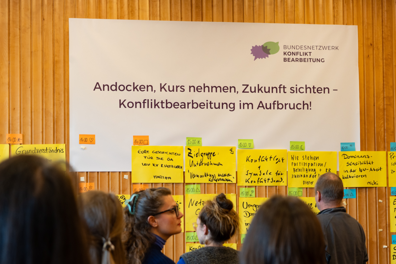 Teilnehmende vor Veranstaltungsplakat und Agenda Bundesnetzwerktreffen