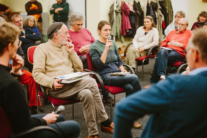 Menschen diskutieren in einer Runde. Eine Frau spricht ins Mikrofon.